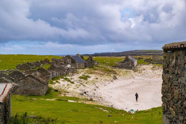 Inishkea_Island_07 old buildings on Inishkea Island and man walking on sand